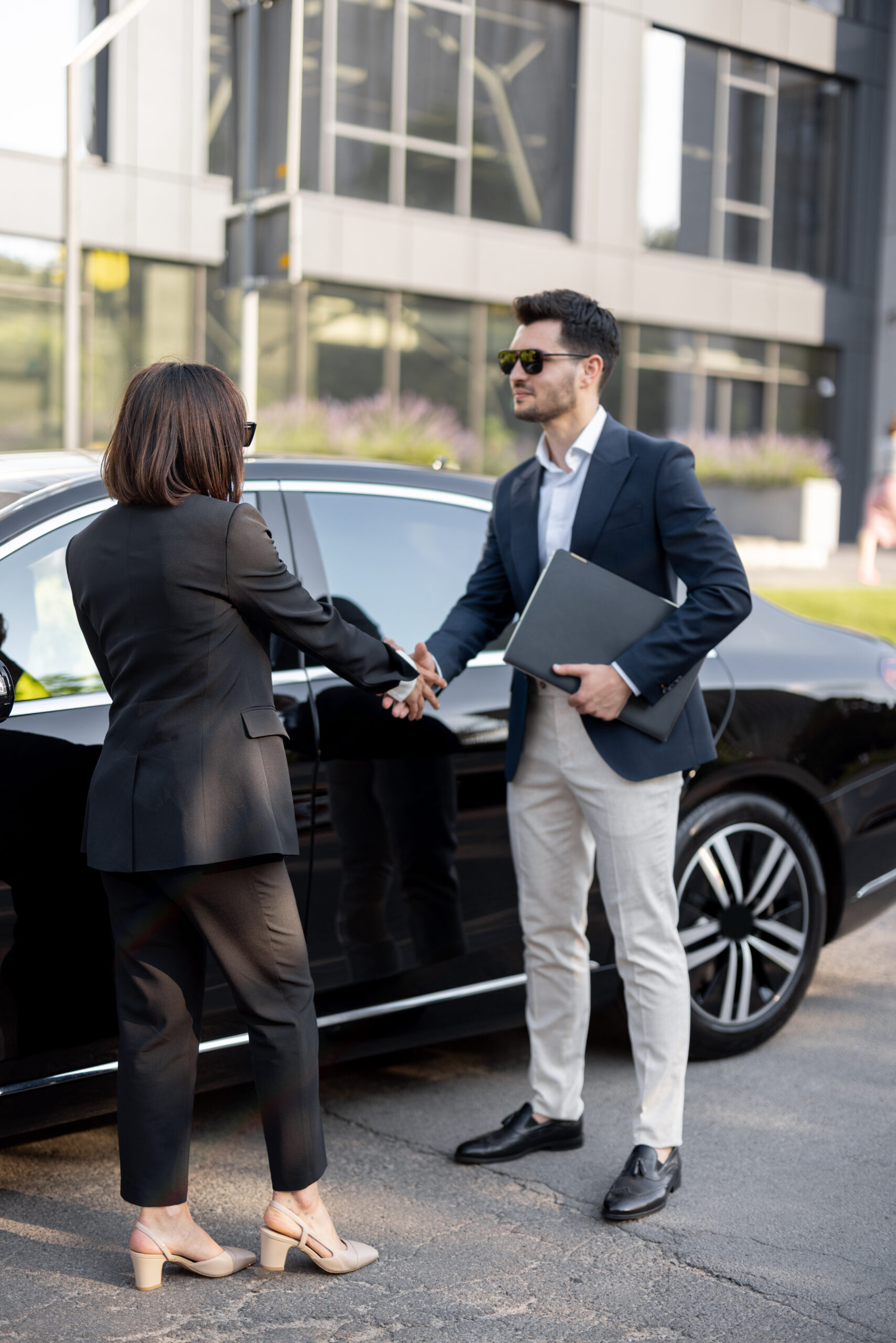 Business man and business woman shaking hands with each other, standing in front of the car outdoors. Concept of successful deal and partnership